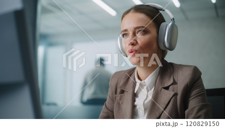 Businesswoman wearing headphones works on computer, chats with business partner 120829150