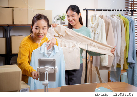 Two young asian woman live online clothing store while showing clothing with tablet and laptop. Two young asian woman live online clothing store while showing clothing with tablet and laptop. 120833108
