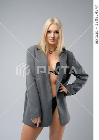 Young woman in oversized blazer and bikini poses against grey backdrop 120834547