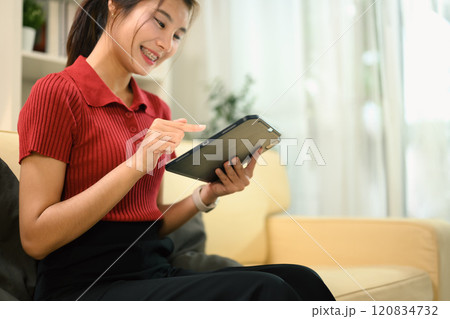Cheerful young woman using digital tablet while sitting on a sofa 120834732