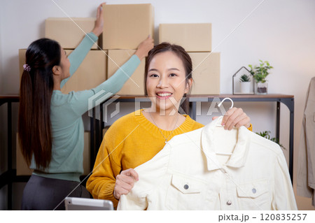Two young asian woman live online clothing store while showing clothing with tablet on social. Two young asian woman live online clothing store while showing clothing with tablet on social. 120835257