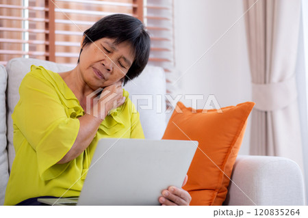 Asian senior woman sitting on sofa with neck pain while using laptop computer in living room at home 120835264