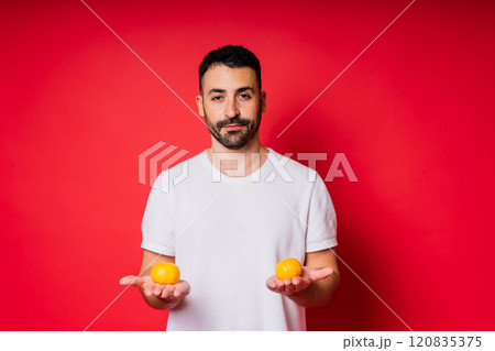 Handsome tall bearded white man with dark hair with tangerine on red background 120835375