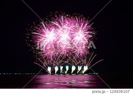 Multi-colored fireworks are launched in the middle of the sea from a large steel ship . 120836107