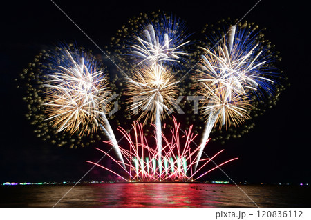 Multi-colored fireworks are launched in the middle of the sea from a large steel ship . 120836112