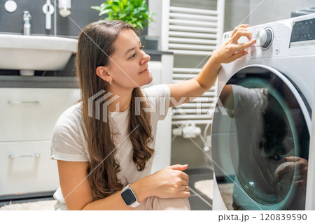 Young woman adjusting washing parameters on washing machine control panel in home bathroom Young woman adjusting washing parameters on washing machine control panel in home bathroom 120839590