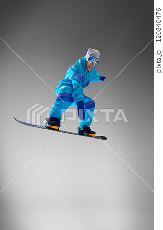 Snowboarder wearing bold outfit, jumps in mid-air against grey studio background, representing essence of seasonal adventures and extreme sports. Snowboarder wearing bold outfit, jumps in mid-air against grey studio background, representing essence of seasonal adventures and extreme sports. 120840476