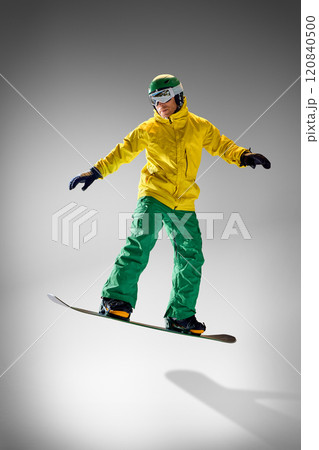 Young athletic man dressed modern, bright yellow and green clothes performing tricks in motion against grey studio background. 120840500