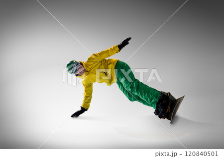 Snowboarder in striking yellow and green attire showcasing his moves in controlled indoor setup, symbolizing focus and winter sports passion. 120840501