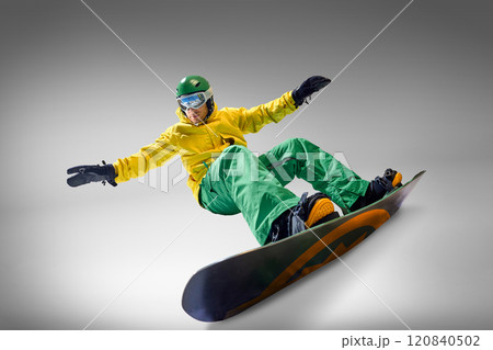 Snowboarder in vibrant yellow and green outfit maintaining balance during snowboarding session, against grey background representing adventure and skill. 120840502