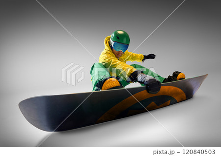 Snowboarder in vibrant yellow and green outfit maintaining balance during snowboarding session, against grey background representing adventure and skill. 120840503