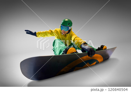 Snowboarder in vibrant yellow and green outfit maintaining balance during snowboarding session, against grey background representing adventure and skill. 120840504