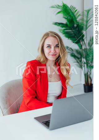 blonde woman in red business suit with laptop online in office at desk blonde woman in red business suit with laptop online in office at desk 120842061