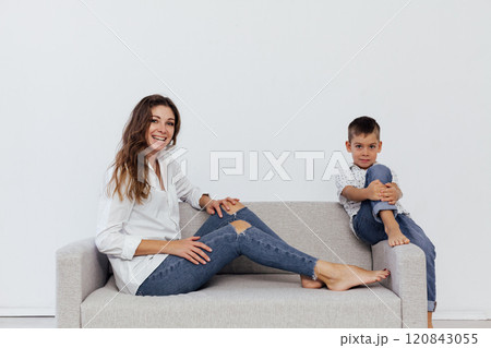 Mom and son sitting on a gray sofa in a white living room Mom and son sitting on a gray sofa in a white living room 120843055