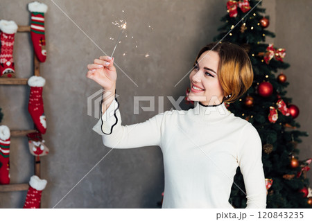 Beautiful woman smiling with sparklers at christmas tree with gifts 120843235