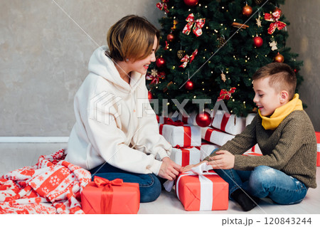 Mom and son decorating Christmas tree with gifts and garlands 120843244
