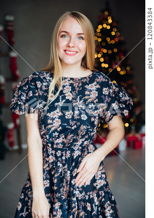 Beautiful blonde woman smiling at Christmas tree with gifts for new year Beautiful blonde woman smiling at Christmas tree with gifts for new year 120843384