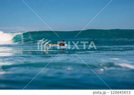 Surfer woman paddling on surfboard in ocean with crashing surfing wave. 120845653