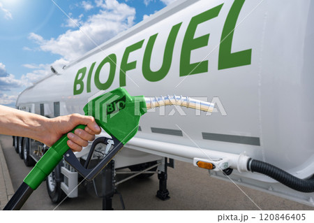 Hand with fuel nozzle with inscription BIO on a background of tank trailer with biofuel. Carbon neutral bio fuel decarbonization concept. Hand with fuel nozzle with inscription BIO on a background of tank trailer with biofuel. Carbon neutral bio fuel decarbonization concept. 120846405
