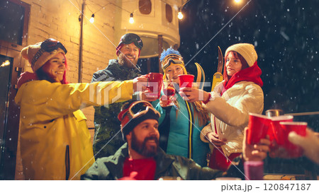 Snowy evening celebration with friends in vibrant ski outfits, raising red cups and enjoying festive gathering filled with laughter and warmth. Snowy evening celebration with friends in vibrant ski outfits, raising red cups and enjoying festive gathering filled with laughter and warmth. 120847187