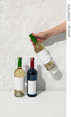 Three wine bottles - two white and one red, and one holding by hand, showcasing variety and elegance for branding projects. Negative space for to insert text, brand name. 120847835