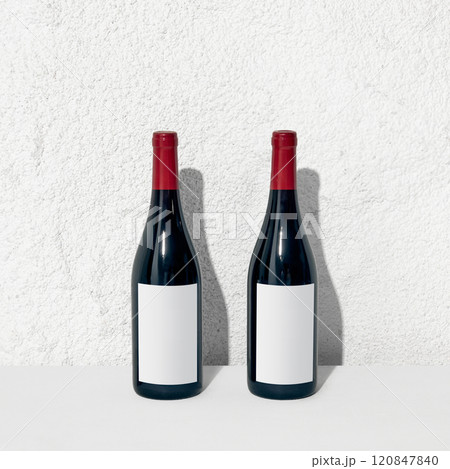Red wine bottle mockup against wall, highlighting its sleek silhouette and blank label for design placement. Copy space for your ad, brand name. 120847840