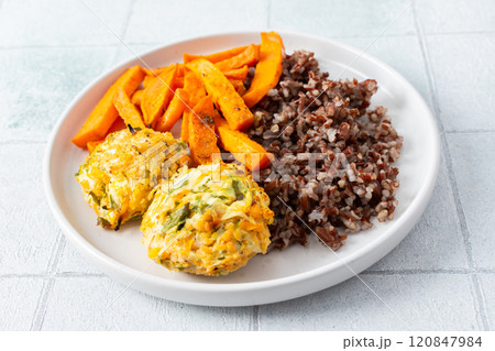 A delicious and wholesome plate featuring brown rice, sweet potatoes, and chickpea pancakes made with squash, perfect for a balanced and nutritious meal, fresh salad of tomatoes and cucumbers 120847984