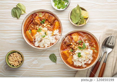 Two bowls of delicious massaman curry with beef, potatoes, rice, and peanuts, garnished with parsley on white wooden background, Thai cuisine Two bowls of delicious massaman curry with beef, potatoes, rice, and peanuts, garnished with parsley on white wooden background, Thai cuisine 120850199