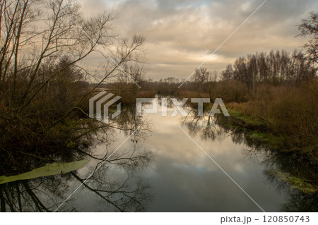 A river with trees that gives a beautiful reflection in the water. A dark sky with clouds in the background 120850743
