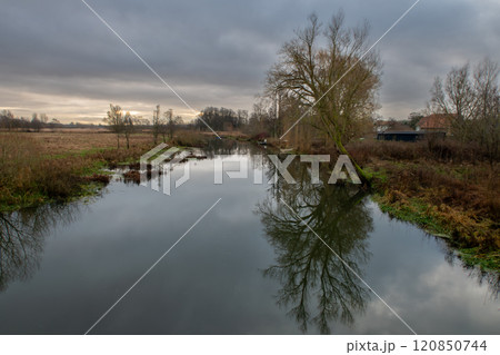 A tree gives a beautiful reflection in a river. A dark sky with clouds in the background A tree gives a beautiful reflection in a river. A dark sky with clouds in the background 120850744