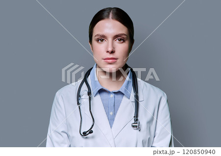 Portrait of young serious woman doctor on gray background 120850940