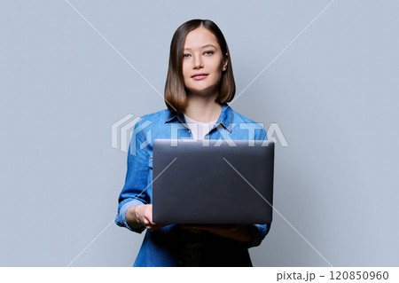 Smiling young woman with laptop on grey studio background Smiling young woman with laptop on grey studio background 120850960