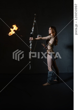 Woman archer demonstrating fire archery skills in a dark studio setting Woman archer demonstrating fire archery skills in a dark studio setting 120850997