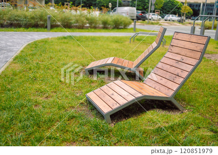 Sun loungers and benches on the lawn with a neatly trimmed lawn without people. Panorama of a well-groomed lawn with beautiful stripes after mowing. Sun loungers and benches on the lawn with a neatly trimmed lawn without people. Panorama of a well-groomed lawn with beautiful stripes after mowing. 120851979