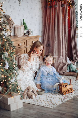 Smiling girl with mom near christmas tree at home Smiling girl with mom near christmas tree at home 120852009