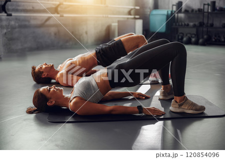 A Couple Engaging in Bridge Exercises Together at a Modern Gym Facility for Fitness 120854096
