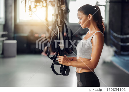 A Focused Woman Diligently Preparing for Her Workout with TRX Straps in the Gym Setting 120854101