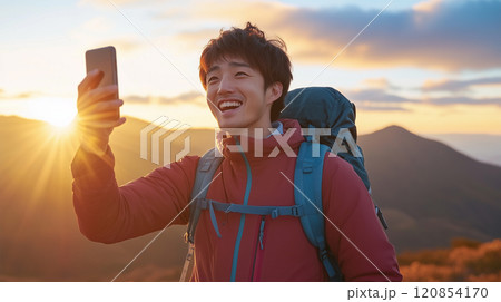 山頂で日の出を背景に自撮りをする日本人男性 120854170