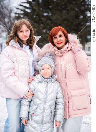 A mother and her two daughters, a teenager and a younger child, enjoy a snowy winter day together. They share laughter and warmth amidst the cold, surrounded by a beautiful, frosty landscape 120855405