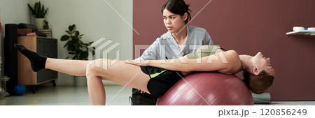 Assisting Woman in Gym With Exercise Ball Assisting Woman in Gym With Exercise Ball 120856249