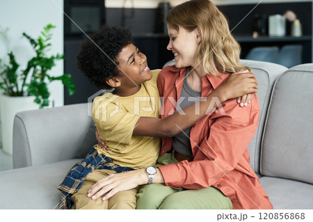 Smiling Child Embracing Caregiver on Cozy Sofa 120856868