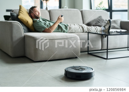 Relaxing on Sofa Using Smartphone While Robot Vacuuming 120856984