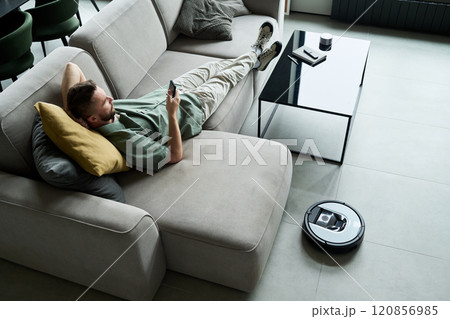 Relaxing on Couch With Smartphone and Robotic Vacuum Nearby Relaxing on Couch With Smartphone and Robotic Vacuum Nearby 120856985