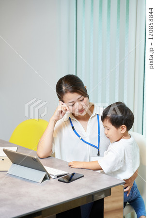 子供を抱えて仕事をする女性 120858844