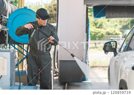 高圧洗浄機の洗車ガンを使い洗車するつなぎを着た整備士の男性 高圧洗浄機の洗車ガンを使い洗車するつなぎを着た整備士の男性 120859719