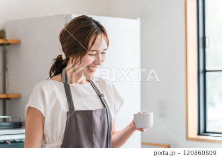 キッチン・ダイニングでコーヒーを飲むエプロン姿の若いアジア人女性 120860809
