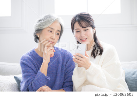 リビングで笑顔で話す、スマホを見ながら過ごす仲良し親子 母と娘のクローズアップ リビングで笑顔で話す、スマホを見ながら過ごす仲良し親子 母と娘のクローズアップ 120862603