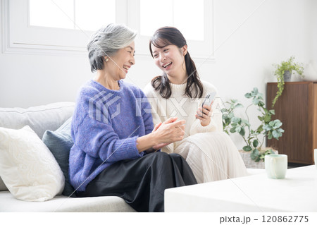 リビングで笑顔で話す、スマホを見ながら過ごす仲良し親子(母と娘)広角	 120862775