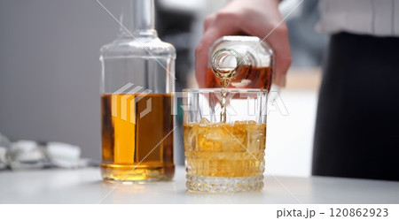 A hand pours a brown alcoholic drink into a glass 120862923