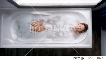 A young woman lies in a soapy foam bath, top view 120863024